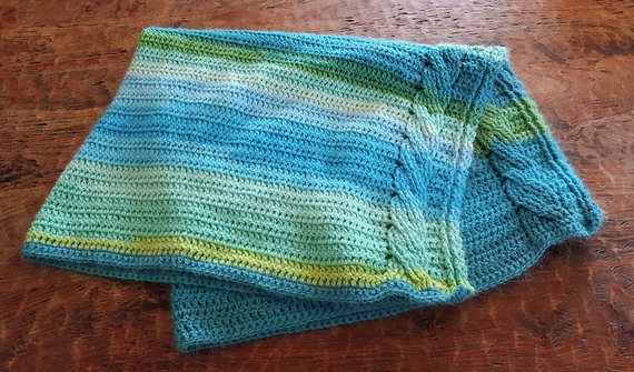 Folded crocheted blanket in blue and green stripes with a cable along the edge
