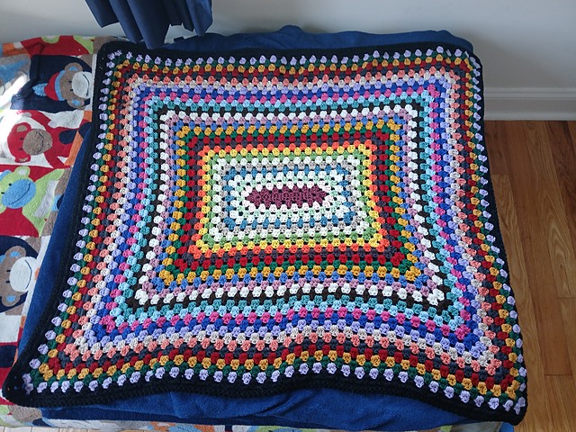 Rectangular granny-stitch blanket in rainbow rounds with a black border
