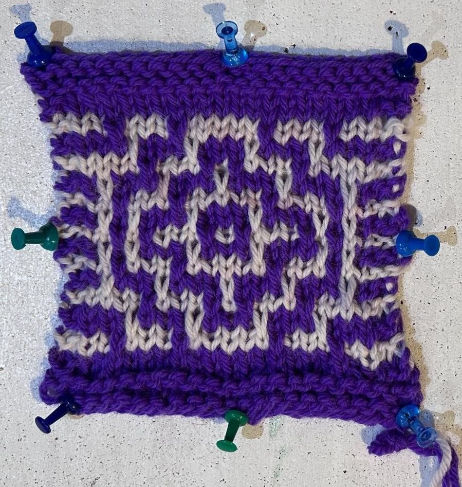 Purple and white knitted mosaic swatch pinned flat, same motif as the crochet swatch